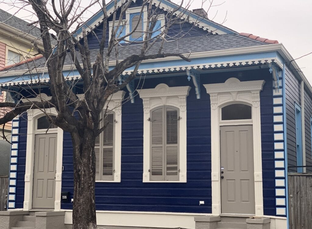 Vibrant and colorful homes lining the streets of New Orleans, showcasing a kaleidoscope of hues and tones. Dark blue with ivory trim house.