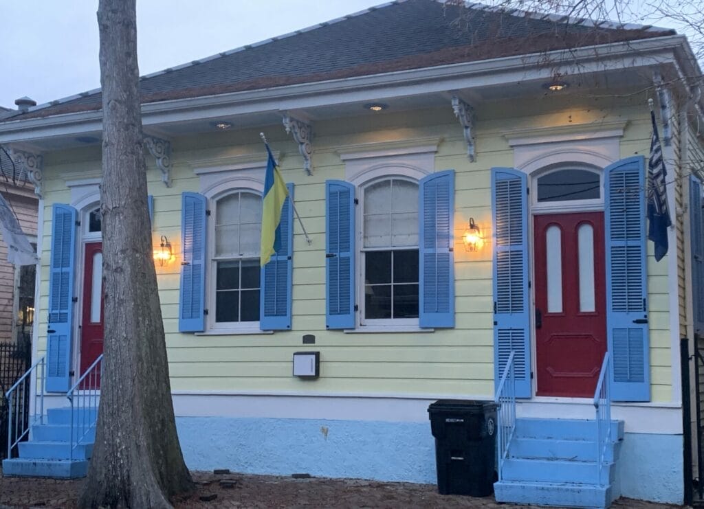 Vibrant and colorful homes lining the streets of New Orleans, showcasing a kaleidoscope of hues and tones. Cream house with blue shutters and red door.