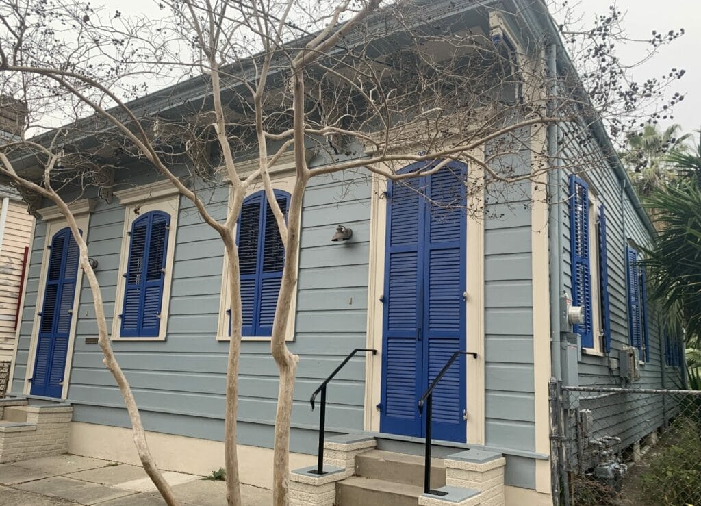 Vibrant and colorful homes lining the streets of New Orleans, showcasing a kaleidoscope of hues and tones. Calm grey blue with dark blue doors home.