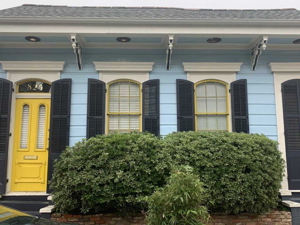 Vibrant and colorful homes lining the streets of New Orleans, showcasing a kaleidoscope of hues and tones. Light blue home with peach trim and dark shutters.