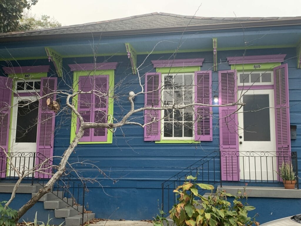 Vibrant and colorful homes lining the streets of New Orleans, showcasing a kaleidoscope of hues and tones. Blue with purple and neon green home.