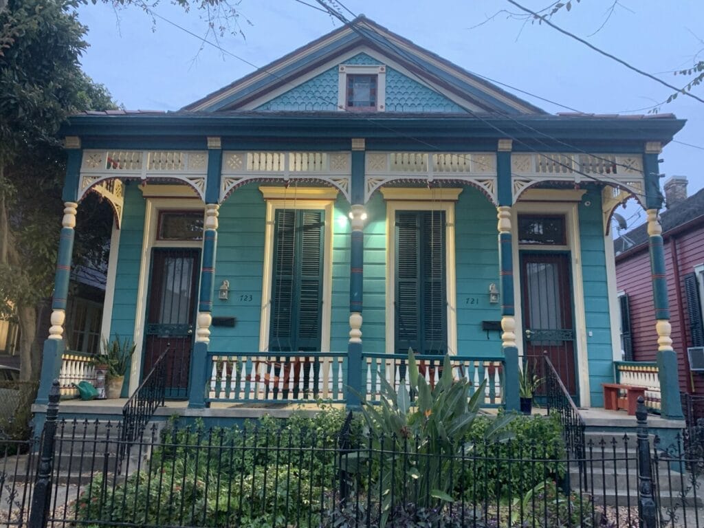 Vibrant and colorful homes lining the streets of New Orleans, showcasing a kaleidoscope of hues and tones. Teal house with inviting blue patio.