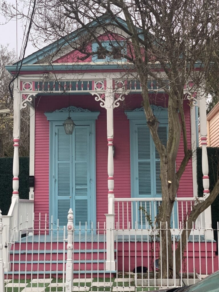 Vibrant and colorful homes lining the streets of New Orleans, showcasing a kaleidoscope of hues and tones. Flamingo pink with delicate columns and trims.