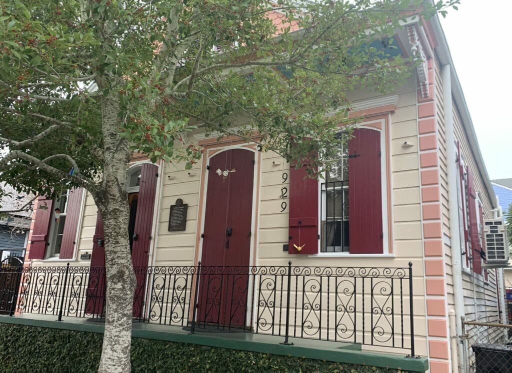 Vibrant and colorful homes lining the streets of New Orleans, showcasing a kaleidoscope of hues and tones. Cream house with pink trim and red doors and shutters.