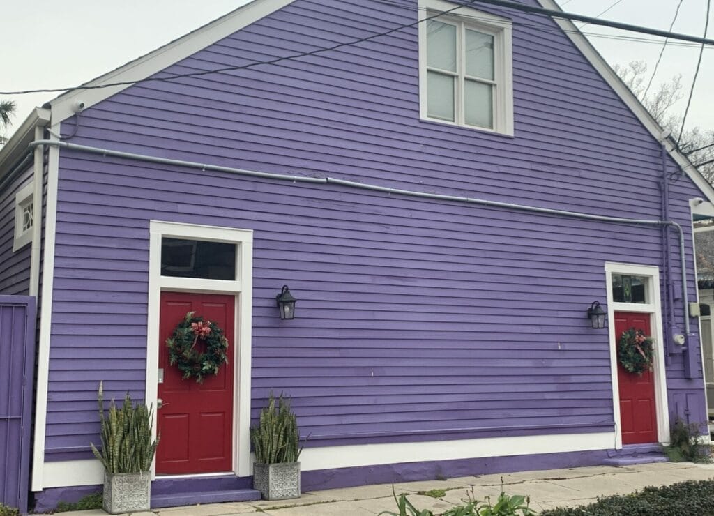 Vibrant and colorful homes lining the streets of New Orleans, showcasing a kaleidoscope of hues and tones. Purple big barn style duplex home with red doors.