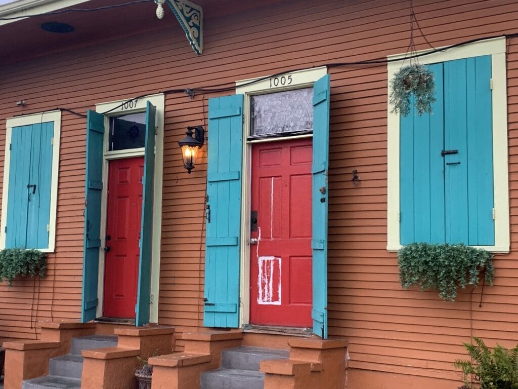 Vibrant and colorful homes lining the streets of New Orleans, showcasing a kaleidoscope of hues and tones. Orangy brown home with red doors and blue shutters sure stands out.