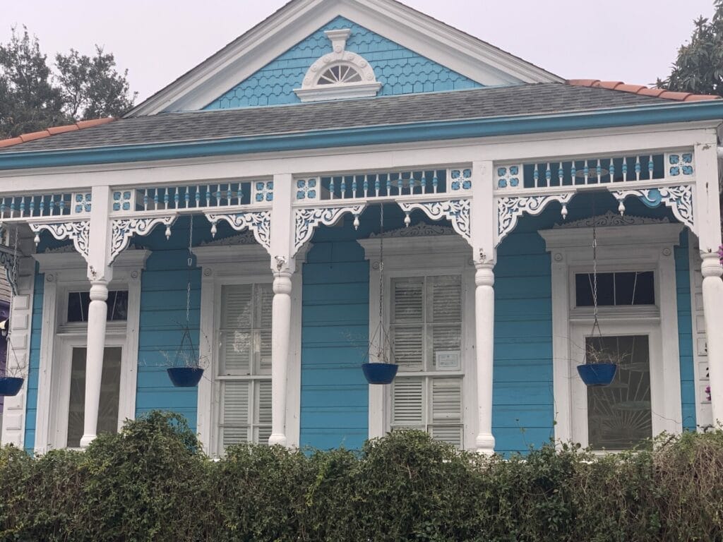 Vibrant and colorful homes lining the streets of New Orleans, showcasing a kaleidoscope of hues and tones. Blue home with white column and delicate trim.