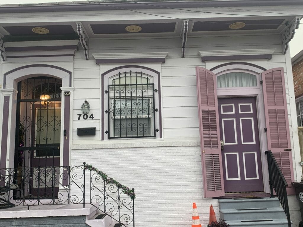 Vibrant and colorful homes lining the streets of New Orleans, showcasing a kaleidoscope of hues and tones. White cottage with deep purple doors.