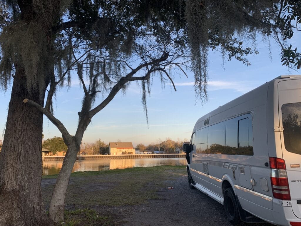 Van parked by the channel under trees with Spanish moss, sunset colors shining on homes across the water.