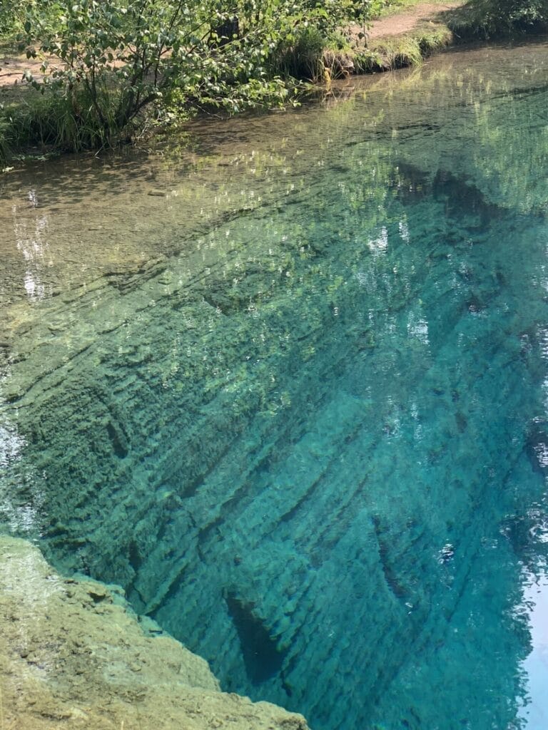 Beautiful blue and clear body of water on the showing the bank of the water is a sheer cliff down deep.