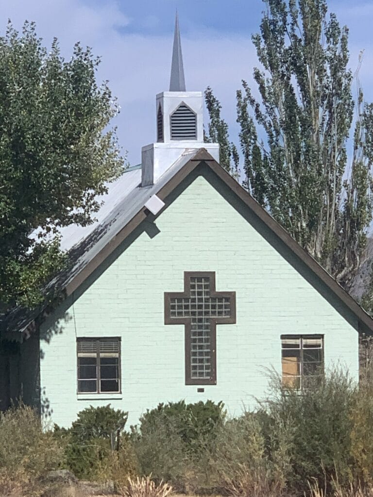 Photo of a charming Little Green Church with bushes in the front and trees on the sides near Mammoth Lakes Airport.