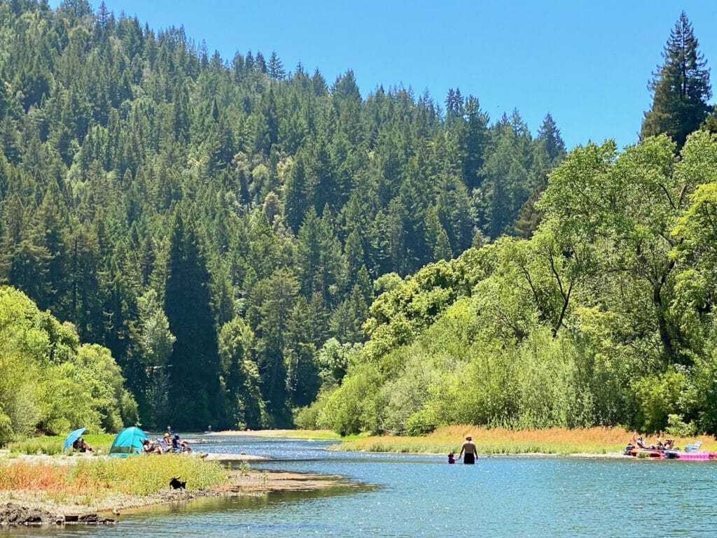 People are in the Russian River, a natural lazy river in Northern California with beautiful forested hill on the bank of the river.