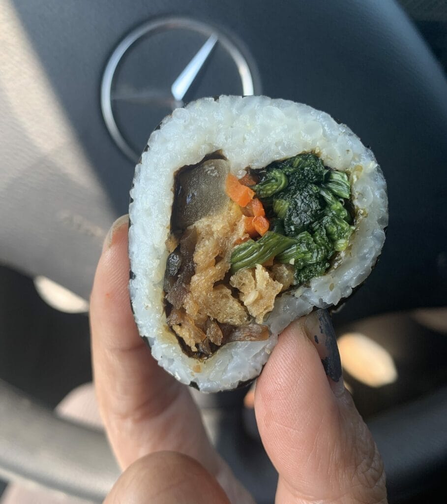 Lillian Lu holding a piece of Costco's vegan Kimbap in their Mercedes Sprinter Winnebago van.