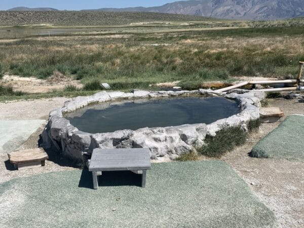 Picture of the Hilltop Hot Springs pool with small stools and grassy rugs around the pool.