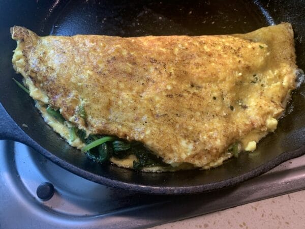 JUST egg omlette is vegan egg alternative with spinach inside on a cast iron pan.