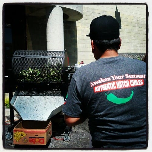 A man tending to the roasting of Hatch chiles with the shirt that says Awaken Your Senses! Authentic Hatch Chiles