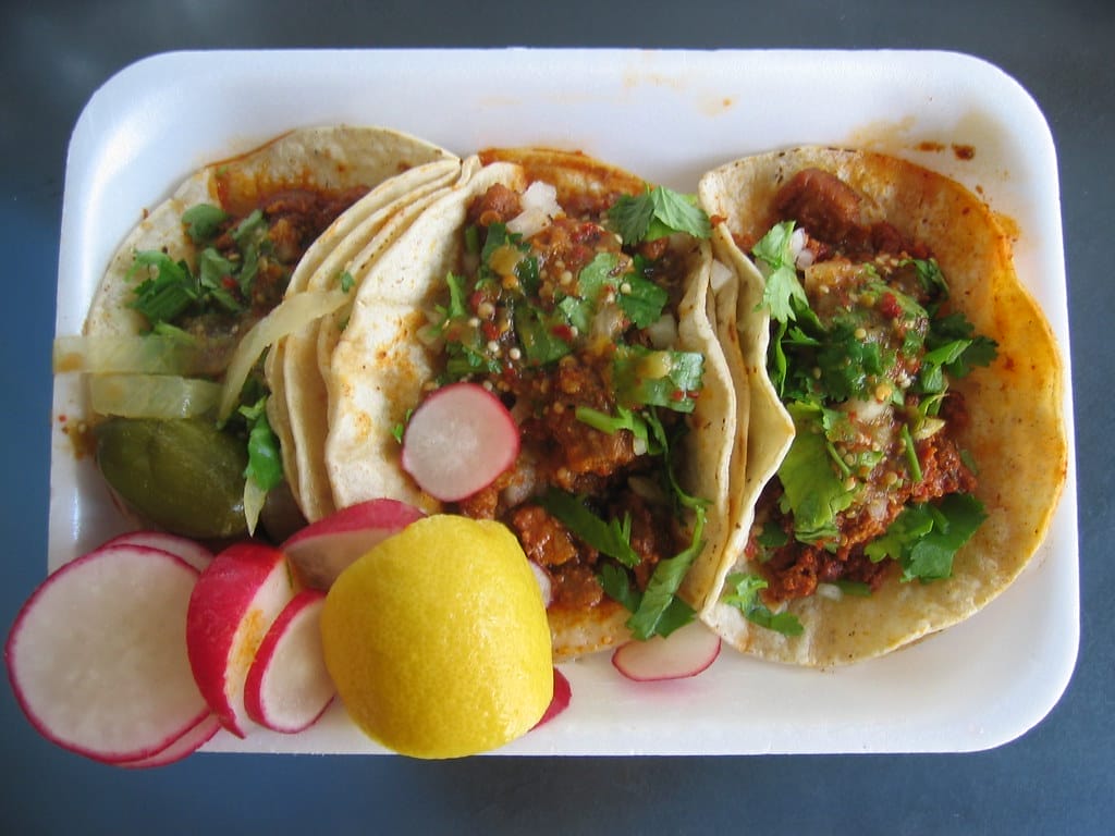 3 sweet potato and Hatch chiles tacos on a plate served with sliced radish and a slice lemon.