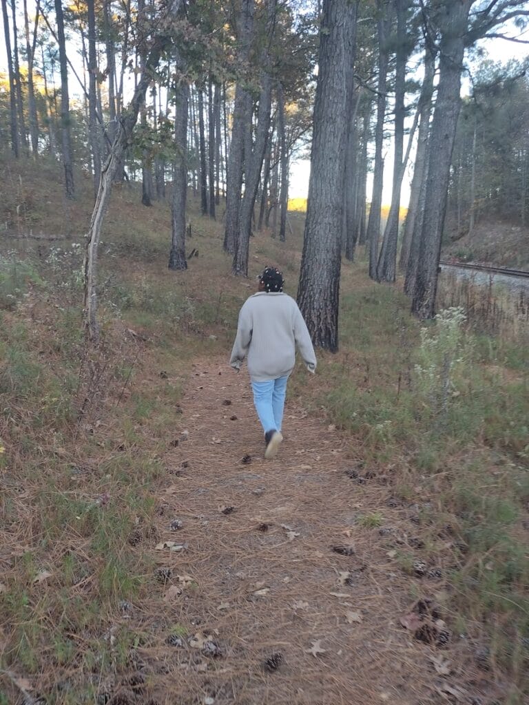 A person hiking in the woods when it's colder, wearing a sweater and the trees didn't have any leaves.