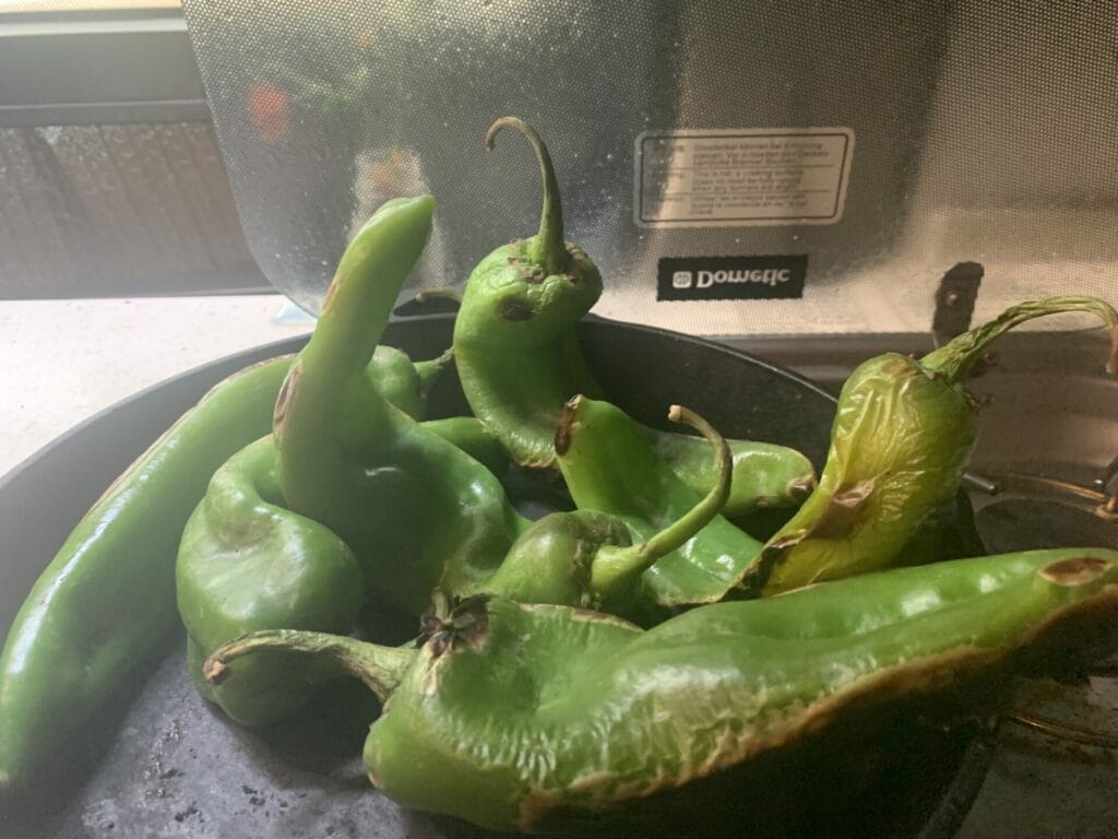 Some Hatch chiles are being roasted on cast iron pan in Lillian's van. Chiles are wiggly and almost statue like.