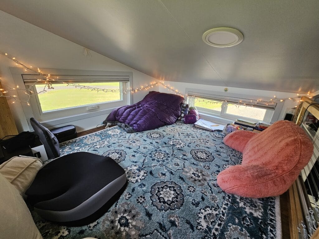 A loft with a rug and different cushions and hanging lights making a small place feel very spacious and comfortable.