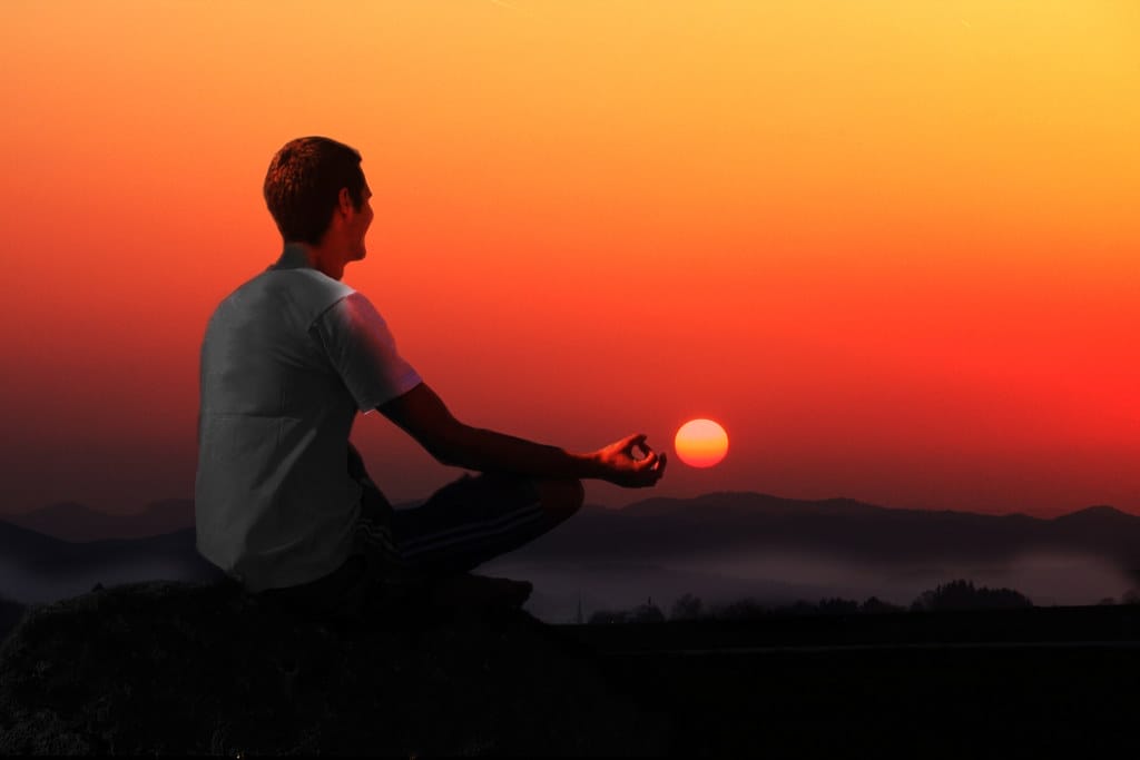 A man in meditation posture with the sunset scenery in the back.