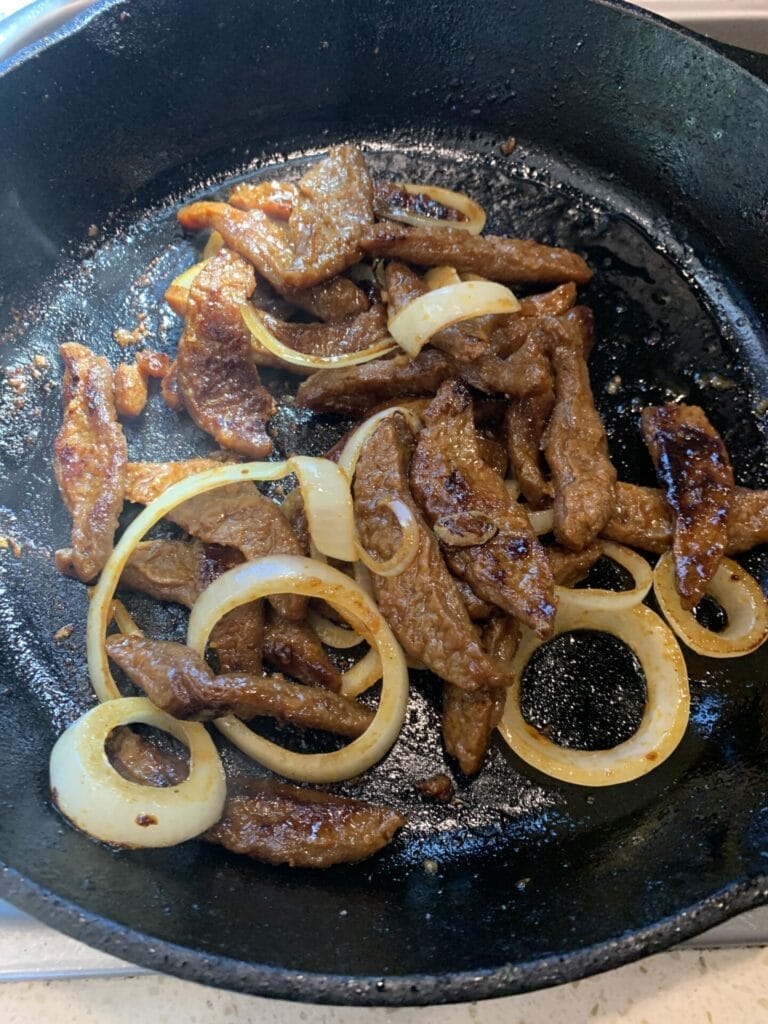 Bobmoos Korean BBQ review as the picture shows the cooked bulgogi with sliced onion in a cast iron pan.