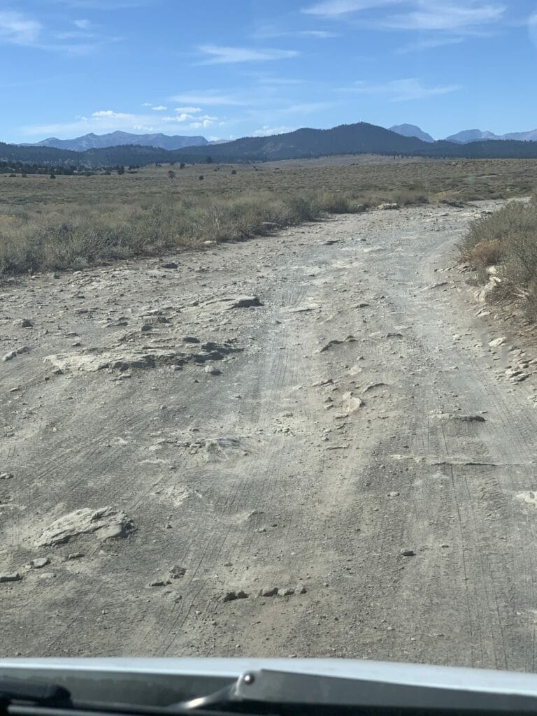 A dirt road that has a lot of rocks and dips with grassy sides of the road is the way to Crab Cooker Hot Springs near Mammoth Lakes, California.