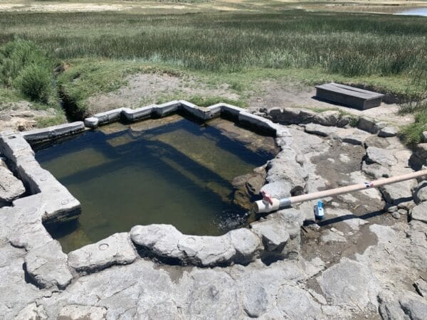 Hot tub made out of rocks and cement in a field of greens is the Shepherd Hot Springs Mammoth in Eastern Sierra.