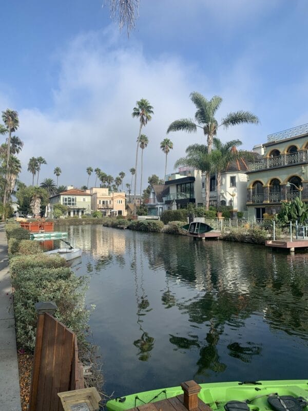 Charming waterway with beautiful homes lining it. Sky is blue with some puffy clouds and water is reflecting the palm trees and homes.