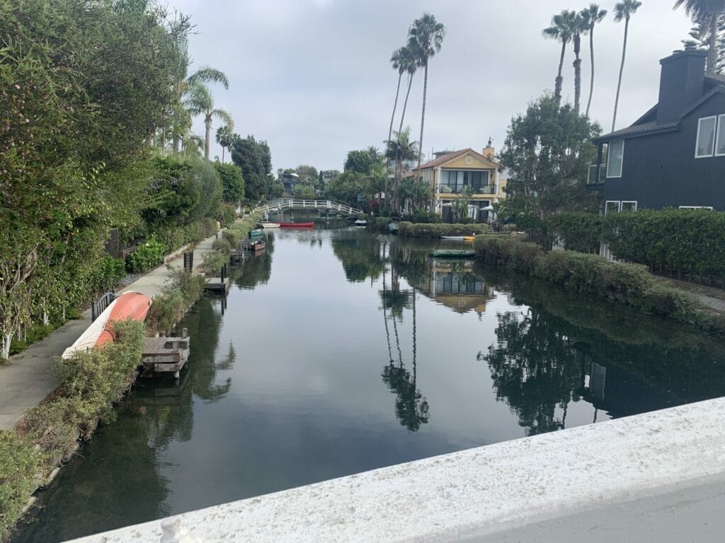 Waterway photo with lined lush trees, walkway, walking bridges and homes. 