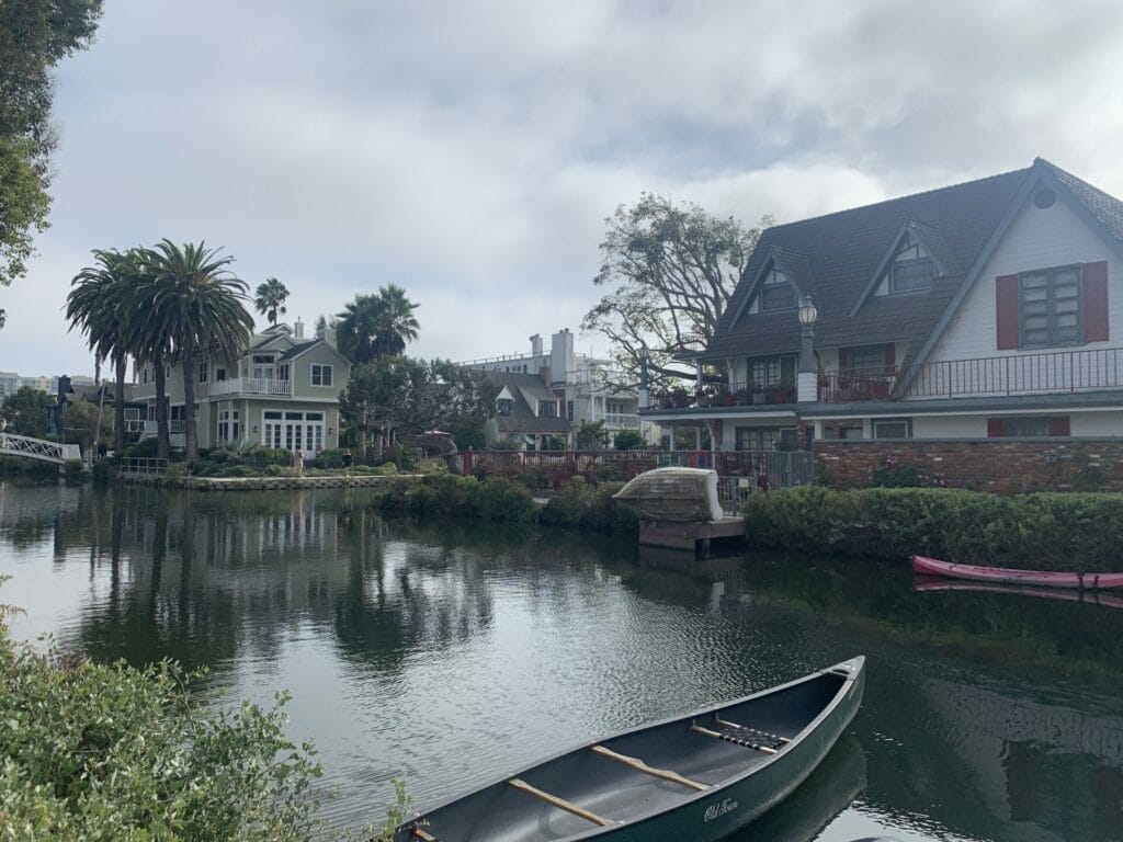 A boat on the water with homes and lush gardens lining the canal in Venice Canals in California.