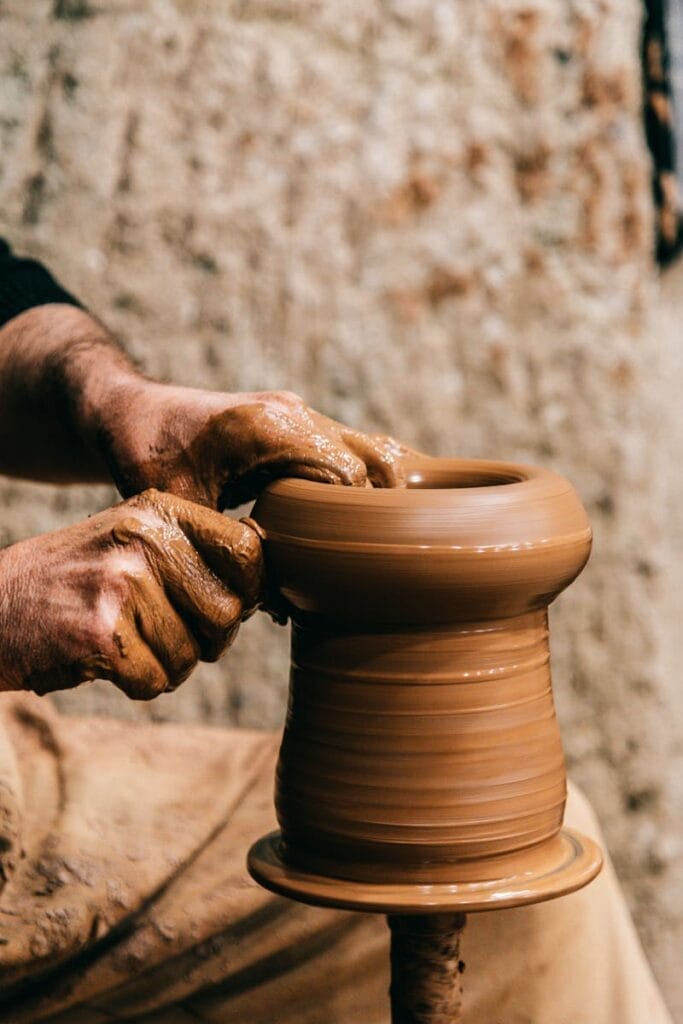 Person creating clay vase while working with pottery wheel on blurred background. Art therapy is one of the unconventional stress relief techniques.